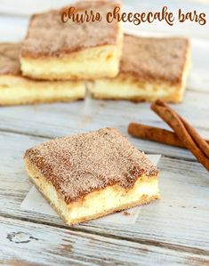 three pieces of cheesecake bars sitting on top of a wooden table next to cinnamon sticks