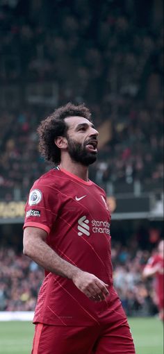 a man in red soccer uniform standing on a field with his mouth open and eyes closed