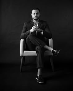 a black and white photo of a man sitting in a chair with his legs crossed