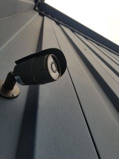 an outdoor security camera mounted on the side of a building's roof, looking up at the sky