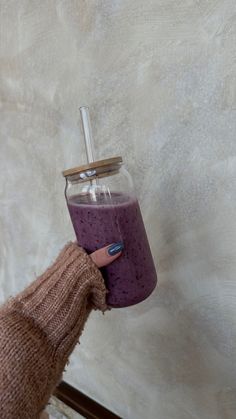 a person holding a purple drink in a glass jar with a straw sticking out of it