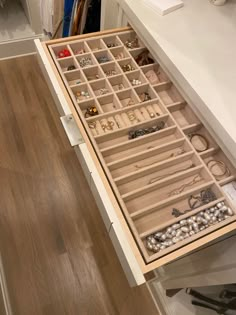 an open drawer in a closet filled with necklaces and bracelets sitting on top of a wooden floor