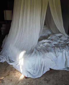 an unmade bed with white drapes on it's headboard and foot board