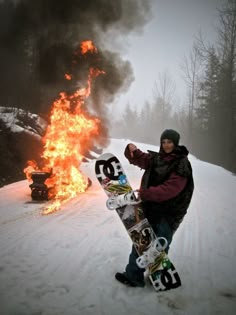 a man holding a snowboard in front of a fire