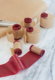 several rolls of red tape sitting on top of a table next to scissors and paper