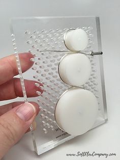 a person is holding two white buttons on a clear plastic object with holes in it