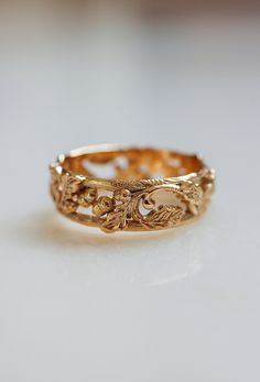 a gold ring with filigrees and leaves on the inside, sitting on a white surface