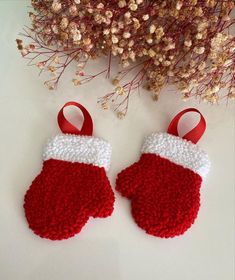 two red and white knitted mittens sitting on top of a table next to flowers