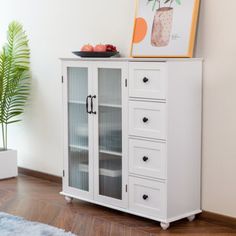 a white cabinet sitting on top of a wooden floor next to a potted plant