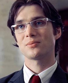 a man wearing glasses and a suit with a red tie is looking at the camera