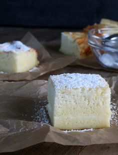 two pieces of cake sitting on top of brown paper next to a bowl of powdered sugar