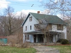 an old white house sitting in the middle of a field with trees and grass around it