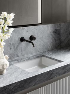 a white vase with flowers in it sitting on a marble counter top next to a sink