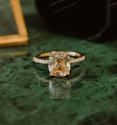 an engagement ring with a yellow diamond in the center on a green table next to a gold frame