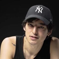 a close up of a person wearing a baseball cap with a black shirt and necklace