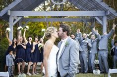 a bride and groom kissing in front of their wedding party at the end of an outdoor ceremony