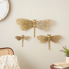 three gold dragonflys are hanging on the wall next to a chair and clock