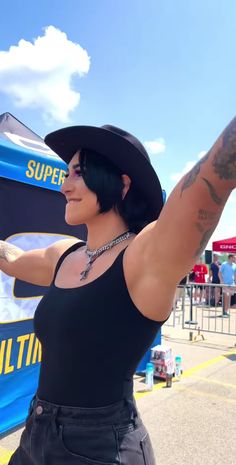 a woman in a black top is holding up her arm and wearing a cowboy hat