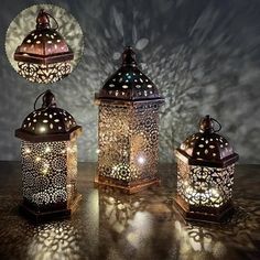 three lit lanterns sitting on top of a table next to each other in front of a dark background