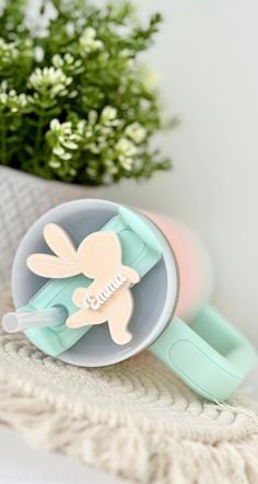 a cup and spoon sitting on top of a table next to a flower pot with flowers in the background