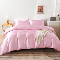 a bed with pink sheets and pillows on top of it, next to a dresser