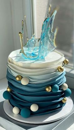 there is a blue and white cake with gold decorations on the top, sitting on a table