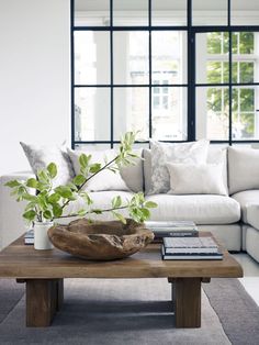 a living room with white couches and pillows on top of the table in front of large windows