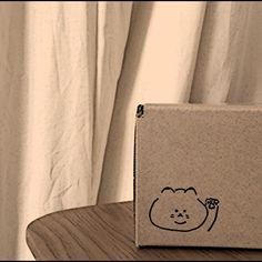 a box sitting on top of a wooden table next to a white curtained window