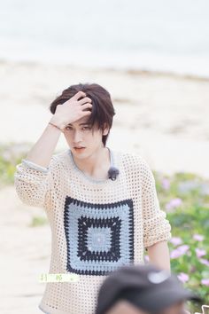 a young man holding his head while standing next to a beach with flowers in the background