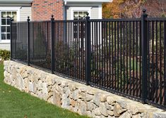 a black iron fence is in front of a house with a stone wall and green grass