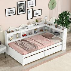 a white bed with drawers underneath it and pictures on the wall behind it in a pink room