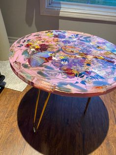 a table with flowers painted on it sitting in front of a window and wooden floor