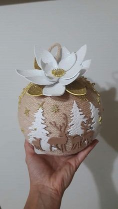 a hand holding an ornament decorated with white flowers and gold foiling on it