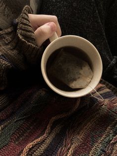 a person holding a cup of coffee on top of a blanket