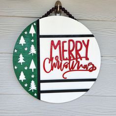 a merry christmas sign hanging on the side of a wooden wall with white and green trees