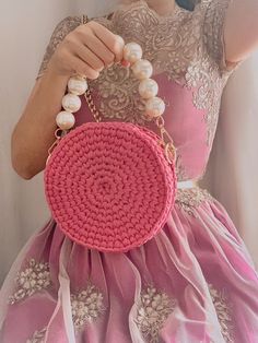 a woman holding a pink purse with pearls on it