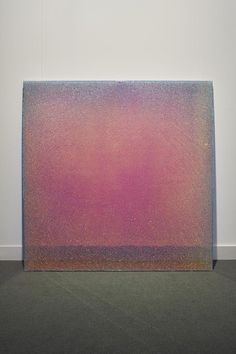 an abstract painting with pink and purple hues on the bottom, against a white wall