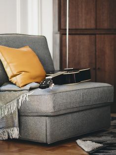 a guitar sitting on top of a gray couch next to a brown pillow and blanket