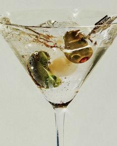 a martini glass with olives and ice on the rim, in front of a white background