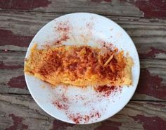 a white plate topped with an omelet covered in red stuff on top of a wooden table