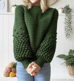 a woman standing in front of a wall wearing a green sweater