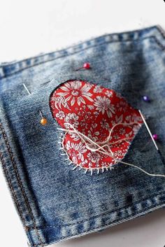 a piece of fabric with pins in it sitting on top of a pair of jeans