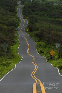 an empty road with yellow painted lines on the side and green hills in the background