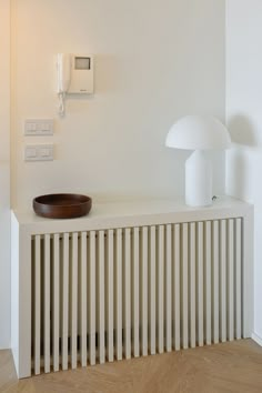 a white radiator with a wooden bowl sitting on it's side next to a lamp