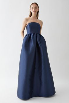 a woman in a strapless blue gown stands with her hands on her hips and looks off to the side