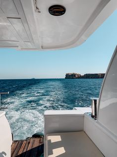 the back end of a boat in the ocean with blue water and land behind it