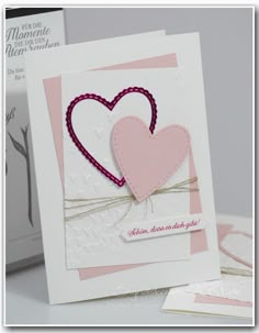 two cards with hearts on them sitting next to each other, one in pink and the other in white