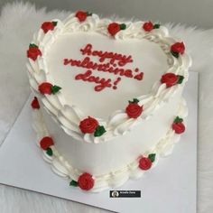 a white heart shaped cake with red roses on the top and writing happy valentine's day