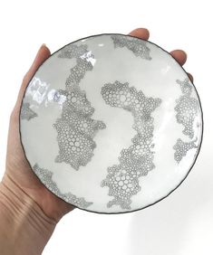 a hand holding a white and black plate with designs on the bottom, in front of a white background