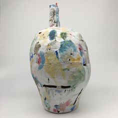 a white vase with multicolored paint splattered on it's side